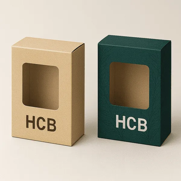 Two rectangular product boxes with clear window cutouts one in plain kraft and the other in dark green with HCB leaf patterns