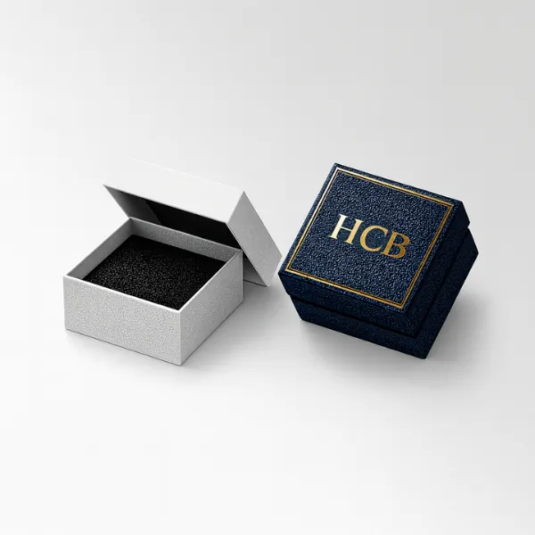 Two small square jewelry boxes - one open in white- one closed in navy with gold HCB lettering-