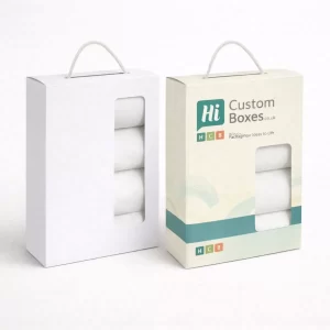 Two vertical retail boxes with rope handles and transparent windows showing folded white linen.