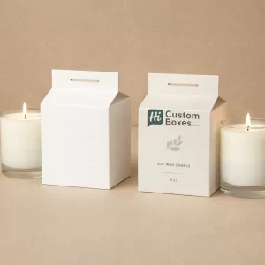 Two white gable-top milk carton style candle boxes with simple leaf motifs and glass candles.