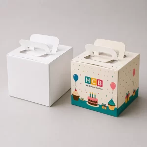 A white square box standing next to a custom printed box with colourful birthday themes.