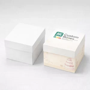 Closed square wedding cake boxes with lids, featuring one plain white and one cream-coloured box with floral designs.
