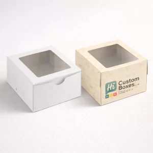 Rectangular white and branded cake boxes with large front windows and sturdy brown handles.