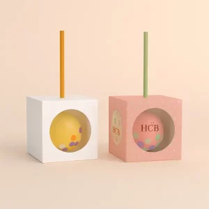 Two cube-shaped cake pop boxes with clear windows - one plain white- one pink with HCB branding and dots