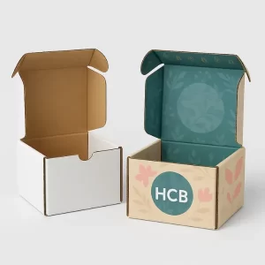 Plain white corrugated mailer box next to a colorful mailer box with teal interior- floral print- and round -HCB- logo on the lid