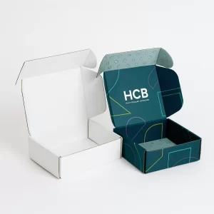 wo open cardboard mailer boxes- One is plain white- and the other is dark teal with geometric graphics and an -HCB- logo on the inside flap